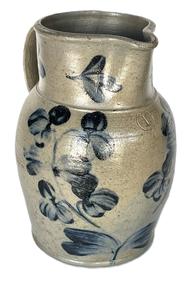 K271 19th century Baltimore, Maryland Peter Herman one gallon Crock Pitcher  stamped I. There is a small hairline crack in the rim. This small stoneware pitcher was made in Baltimore circa 1850 to 1870. It is decorated in cobalt with a two-stemmed flowering plant, along with flowers on the rim and highlights at the handle terminals.  Measurements: 10 ¼ tall. 