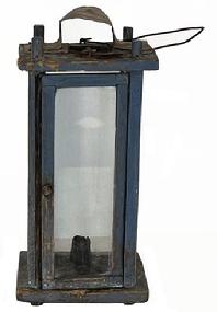 K1503 19th century Pennsylvania original blue painted tall wooden Lantern featuring four bubbled glass panels contained within a wooden pinned and post construction frame.  Door opens freely to access the crudely made metal candle socket. The area above the candle is covered with tin to prevent scorching/burning of the wood. There is a hole in the top for ventilation purposes which is covered on the exterior with a bent piece of sheet metal to create a hood that protects the candle flame from wind/rain. A wire bale handle is attached to the top for carrying/hanging purposes. Two very early metal make-do repairs are present on the top where the hood is attached. The wood is pine. Circa mid-1800s. Measurements: 6 ½ x 6 3/8 x ~13 ½ tall  not including handle. 