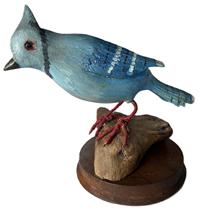 K167 Hand carved wooden Bluejay perched on a small piece of driftwood - signed R. Bernier on bottom. Wonderfully hand carved and painted details with glass eyes, mounted on a 4 ¾ round wooden disk for display purposes. Carver, Ronald Bernier (1873-1952) of Biddeford, Maine was also known as Bernier the Lumberman a lumberman by trade who took up carving after being injured in an accident. Approximate overall measurements:  8 ¼ long x 5 ½ wide x 6 ½ tall.  