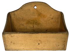 **SOLD** K1647 19th century Pennsylvania wall box with original mustard painted surface. Mrs. K A is carved into the bottom.  Box features a tall, shaped back with hole for hanging purposes and shaped ends with tapered top edges along the front and sides. Small wire nail construction. The wood is a combination of walnut and pine. Circa 1870s. Measurements: 12 ½ wide x 5 ½ deep x 4 ¼ tall (front) x 9 tall (back).  