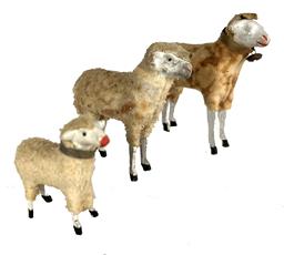 K78C Group of three German Putz Sheep - each with painted eyes, dapple cloth covered composition body with freestanding wooden legs and painted hooves. Two have their collars intact, one also has a bell on its collar. Slight damage visible to his nose and ears of the two larger sheep. Largest to smallest, they stand 4 ¼ tall 3 ½ tall and 2 ½ tall