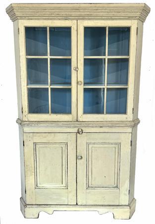 **SOLD** H299 19th century western Maryland white painted corner cupboard. One piece. Features two, six-pane glass doors over two raised panel doors below. All doors are fully mortised and pegged. Tall, applied bracket base with decorative cut outs. Wide, stacked cornice molding adorns the top and around the waist molding in center of the cupboard. Square head nail construction. The wood is white pine. Circa 1830s.