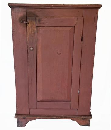 J288 Wonderful early 19th century Pennsylvania one door cupboard in original red painted surface featuring an oversized dovetailed base with cut out feet, applied moldings and a beautiful, raised panel door that is mortised and pegged. Clean interior with sturdy shelves for storage. Square head nail construction. Circa 1810s-1820s. Measurements: 34 wide x 16 ¼ deep x 51 tall. 