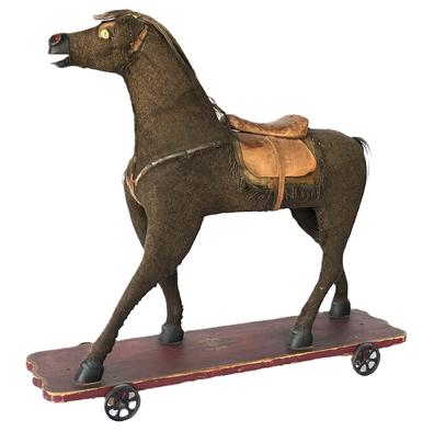 **SOLD** K217 Early 1900s large Pull-Toy Riding Horse on original red painted and decorated wooden platform with metal wheels. The solid wooden horse features hand carved and painted nose/mouth and hooves, a very well-worn mohair covering, glass eyes and leather saddle/tack resting on an original red painted platform with mustard paint decoration and four original metal wheels that move freely.