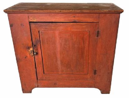 H173 Early 19th century one door Storage Cupboard in original bittersweet red paint. The top of the Cupboard is dovetailed with a single panel door which is mortised and pinned. Door opens to reveal a nice, clean interior with shelves. It has a nice high cut out foot. Original surface. The wood is white pine. Square head nail construction. Circa 1820.   Measurements: 40 1/2" wide x 36" tall x 18 ½ deep. 