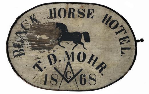 J448 19th century Pennsylvania oval shaped double-sided wooden Trade sign with steamed and bent wooden framed edge advertising "Black Horse Hotel" above a black painted running horse with "T.D. Mohr 1868" painted below. A Masonic compass and square is painted in the center of the date. The lettering is hand done in black paint on a white painted background. The bentwood framing surrounding the sign is painted black. Double-sided, with one side showing a great deal more wear than the opposite side  indicating possible exposure to weather. Remnants of the original hand-forged iron hanger, secured with rosehead nails, remain on one side of the sign. Measurements:  34 wide x 1 7/8 thick x 24 tall.  NOTE: There was a Black Horse Hotel located in Kutztown, PA during this time period however, unfortunately; no evidence of T.D. Mohr could be found as its proprietor  although there were a number of Mohr family members living in that area during the 1860s.