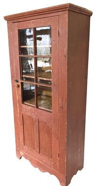 **SOLD** K98 Mid-19th century Eastern Pennsylvania original red painted one door cupboard with applied molding around top and a nice cut out base. The single door is fully mortised and pegged with six original, wavy glass panes in the top over panels below. Square head nail construction. The wood is pine. Clean, natural patina interior.  Circa 1850s. Measurements: 37 &frac14;� wide x 18 &frac12;� deep x 78 &frac14;� tall.   