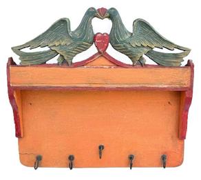 **SOLD** M121 Pennsylvania Folk Art carved and painted hanging rack with original pumpkin, mustard and red painted surface with shaped sides and five (5) forged iron hooks along the bottom edge. The top crest features a cut out Folk Art motif featuring two large carved birds and a heart in original polychrome painted green, red and mustard. The wood is pine with small wire nail construction. Circa 1900-1910. Measurements: 19 3/8� wide x 2 5/8� deep x 18� tall. 