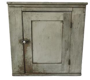 **SOLD** K175 19th century Pennsylvania small hanging corner cupboard bearing original gray painted surface and applied molding along the top. Mortised and pegged door opens to reveal a white painted interior with shelf for added storage. Square head nail construction. The wood is pine.  Circa 1860s-1880s.  Measurements:  27� tall and takes a 19� corner.  