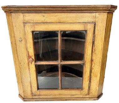 L161 Early 19th century Pennsylvania glass door hanging corner cupboard with applied molding on top and bottom bearing its original mustard painted surface. The four-windowpane door is fully mortised and wooden peg construction with a beaded edge and opens to reveal two butterfly shelves and one straight edge shelf inside. The wood is pine with square head nail construction. Cupboard is 29 &frac14;� tall and takes a 21 &frac12;� deep corner. 